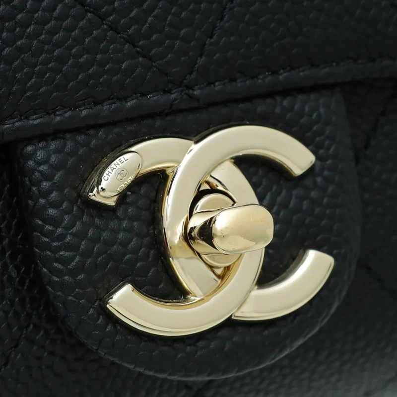 Close-up of a black leather handbag with a prominent gold double C logo clasp, featuring a quilted pattern on the leather.