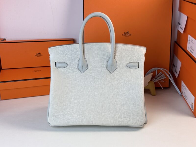 The Hermes Birkin Milkshake White, with its structured shape and textured design, is showcased against a backdrop of multiple orange boxes.